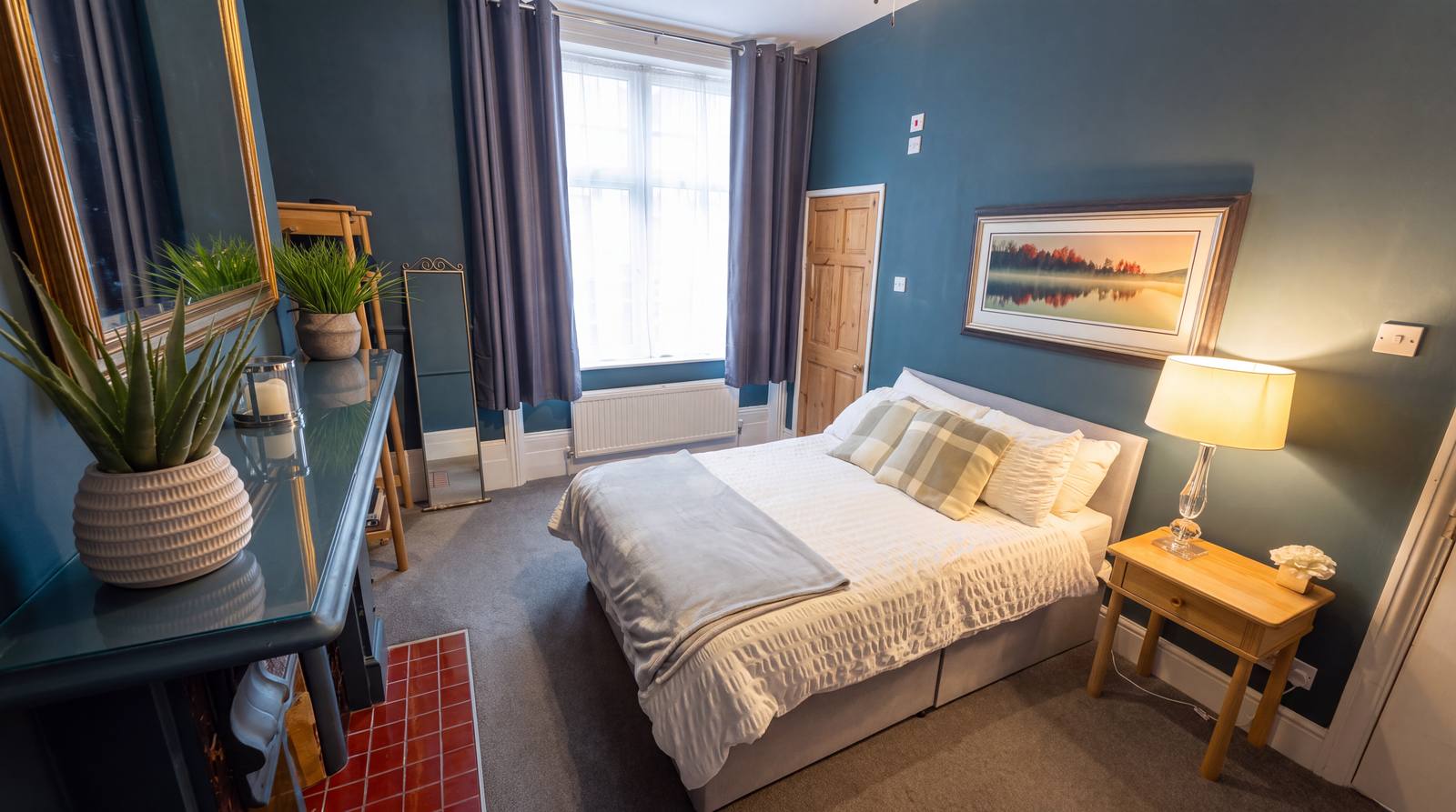 A guest room - a dressing table, plant and a made-up double bed